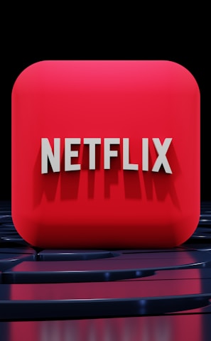 A red, cube-shaped icon with the word 'NETFLIX' prominently displayed in white, bold letters. The cube is set against a dark, glossy, circular patterned background, reflecting a sleek, futuristic design.